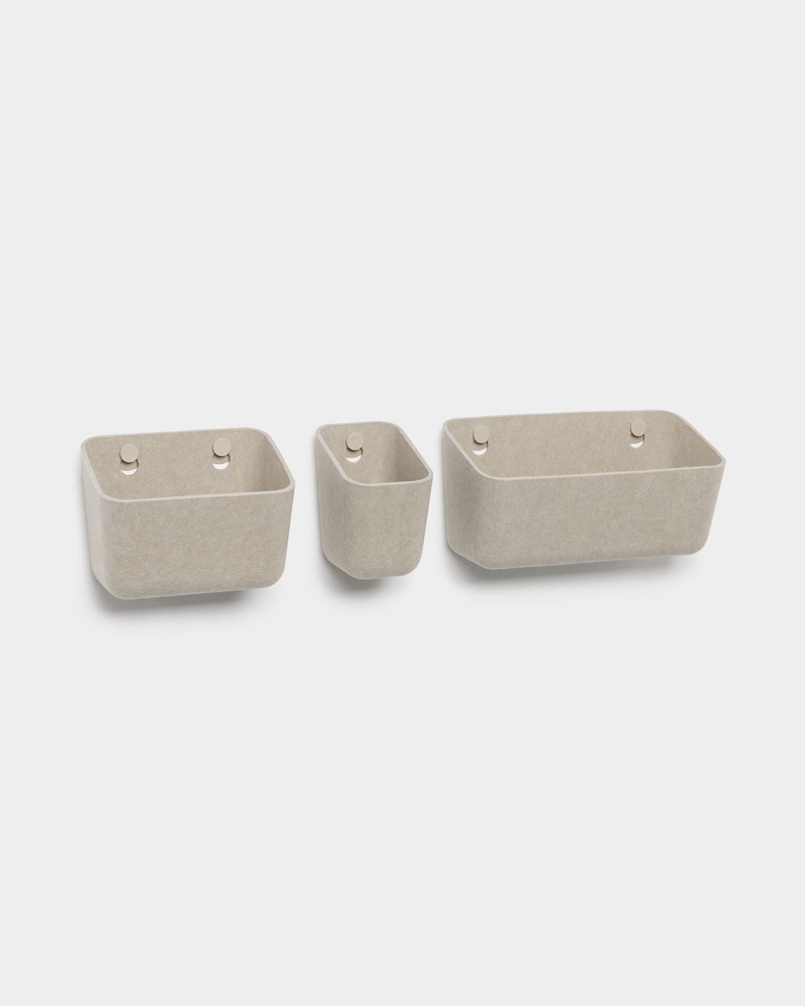 Juego de tres recipientes de fieltro WoodUpp Luva de color beige, cada uno con dos agujeros redondos para colgar, mostrados sobre un fondo blanco.